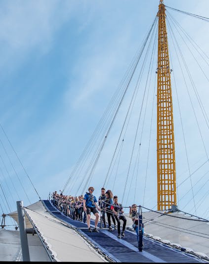 Climbers ascending the O2 Arena roof in London with city skyline in the background.