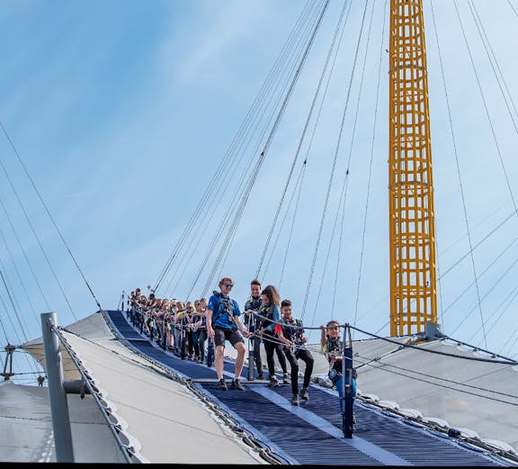 Visitors climbing the O2 Arena roof in London with safety gear.