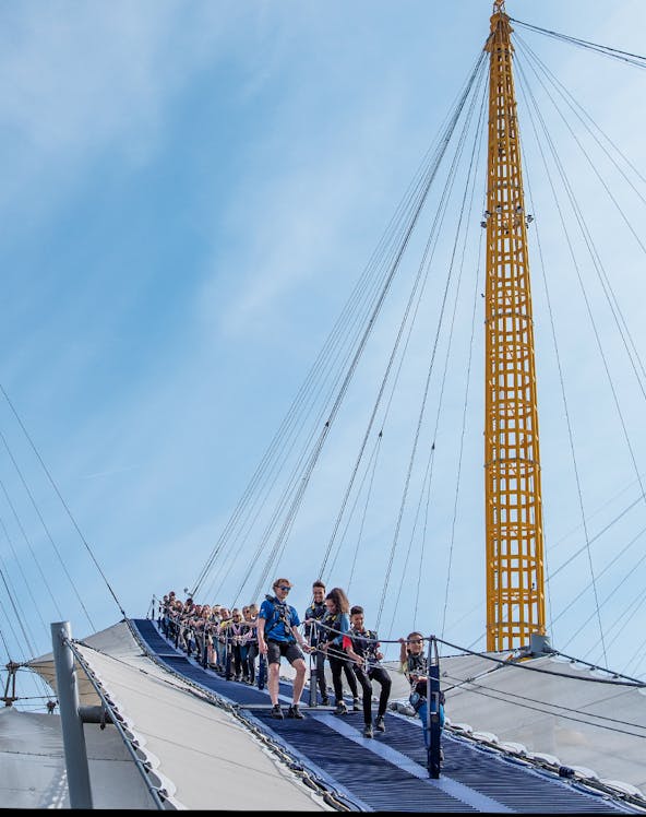 Visitors climbing the O2 Arena roof in London with safety gear.