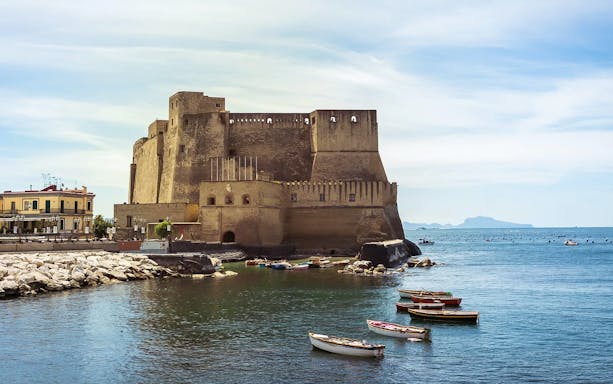 Ovo Castle in Naples, Italy, with boats on the surrounding water.