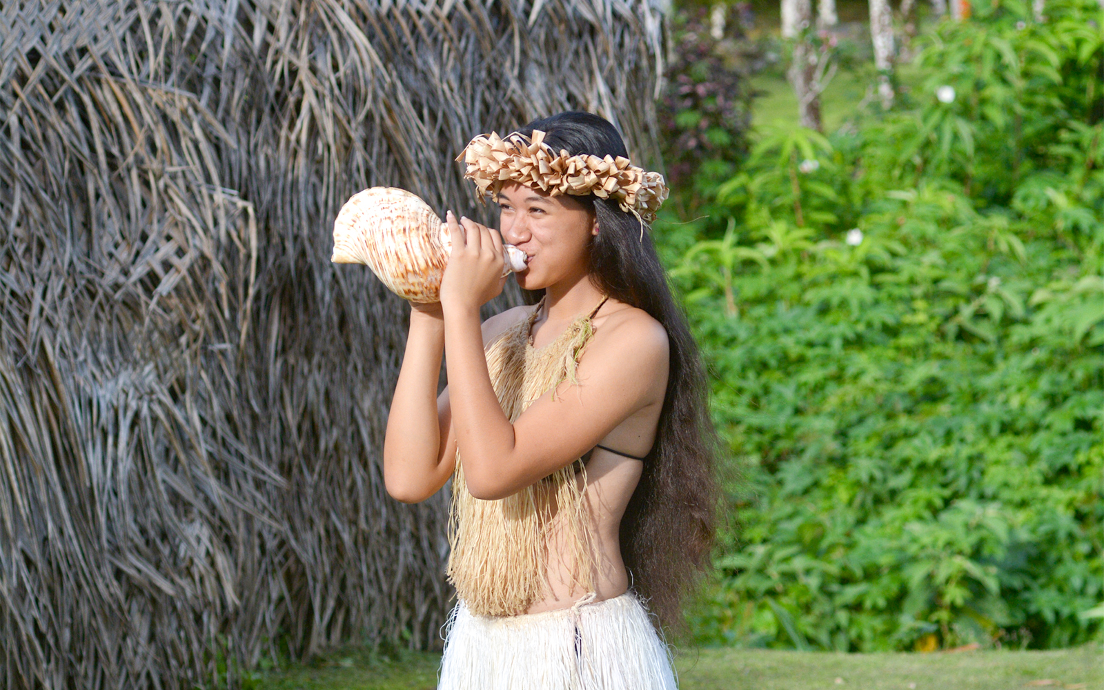 Girl blowing conch shell at luau, Hawaii.