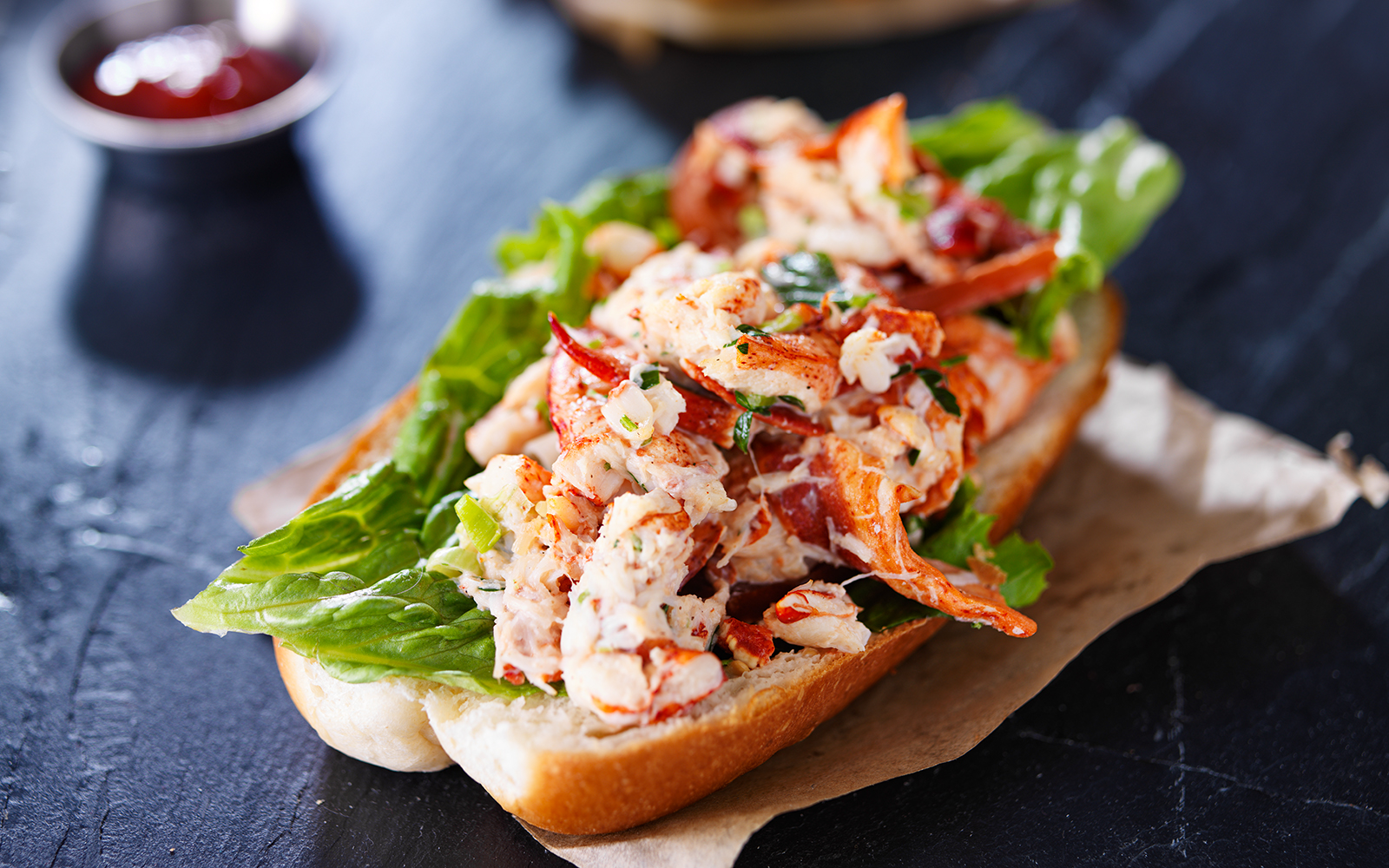 Lobster roll with lettuce on a bun, served on a paper wrapper.