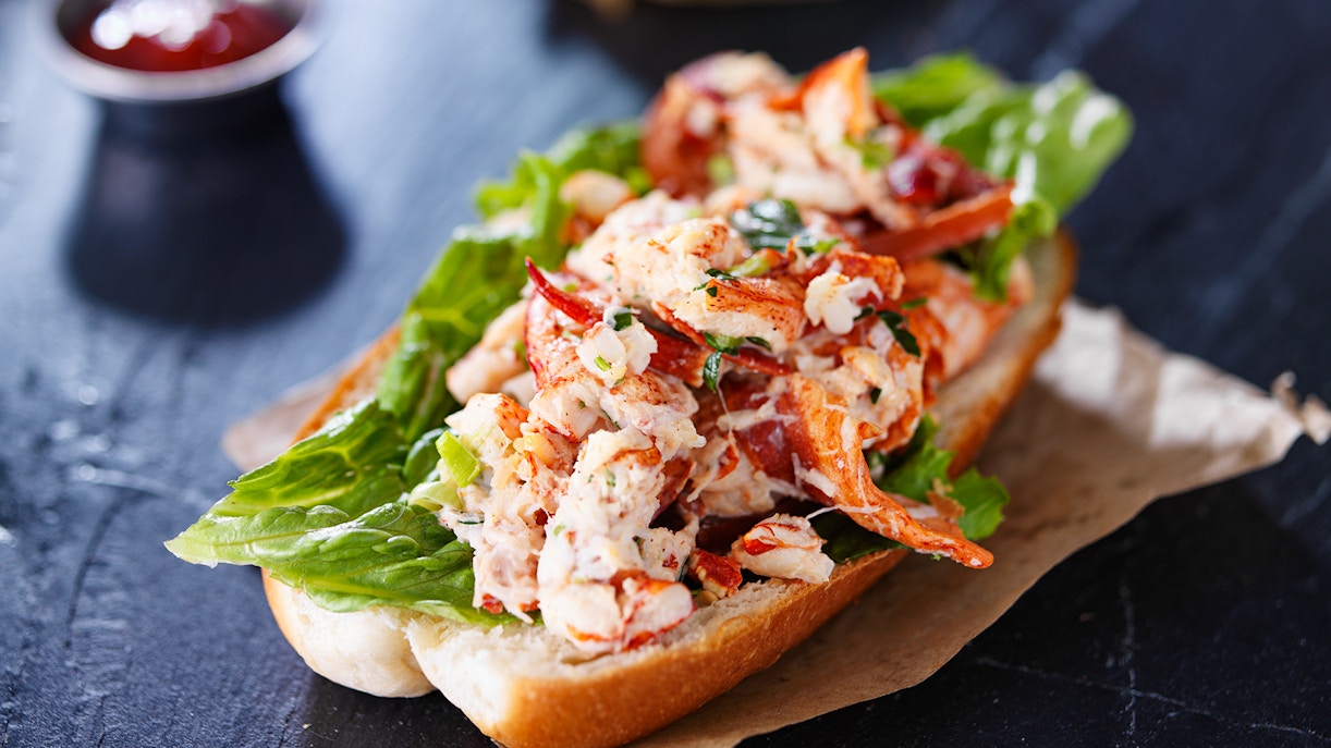 Lobster roll with lettuce on a bun, served on a paper wrapper.