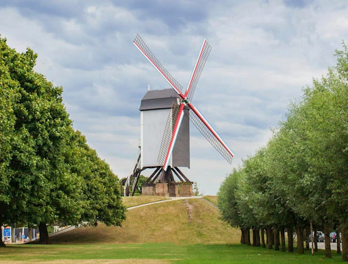 Sint Janshuismolen windmill in Bruges, Belgium, surrounded by green grass and trees.