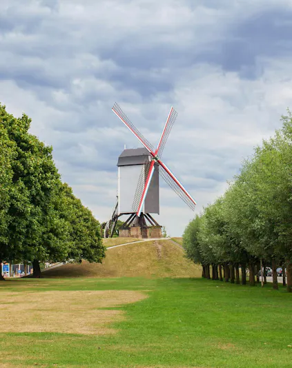 Sint Janshuismolen windmill in Bruges, Belgium, surrounded by green grass and trees.