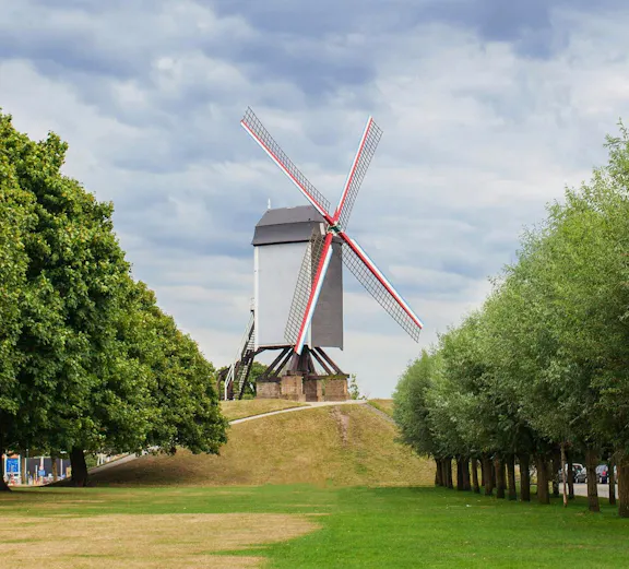 Sint Janshuismolen windmill in Bruges, Belgium, surrounded by green grass and trees.