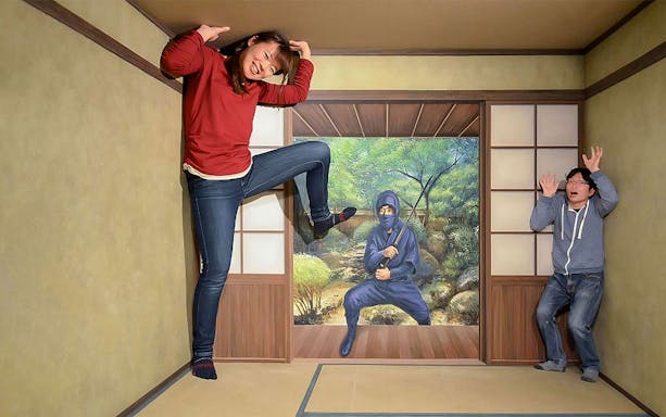 Visitors interacting with ninja-themed optical illusion at Tokyo Trick Art Labyrinth Museum.