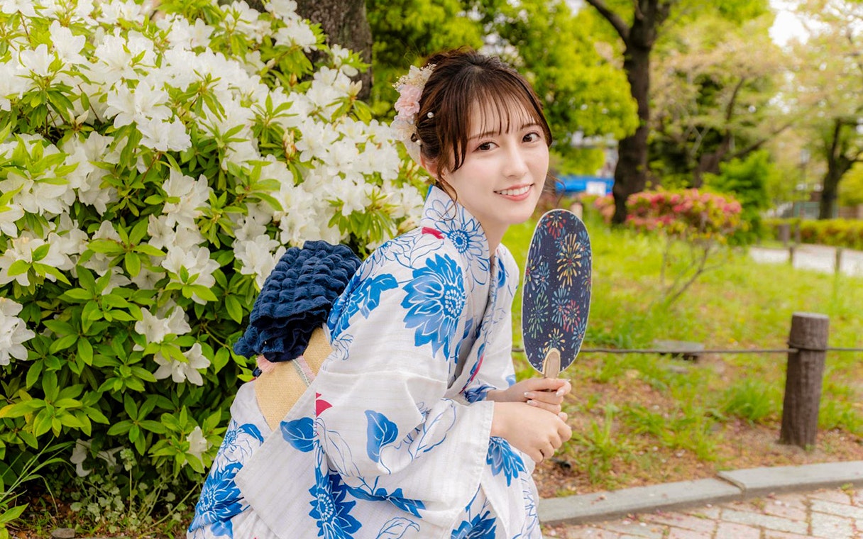Tourist in Yukata holding fan near blooming flowers in Japan.