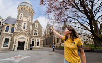 Person pointing at historic stone building in Christchurch during walking tour.