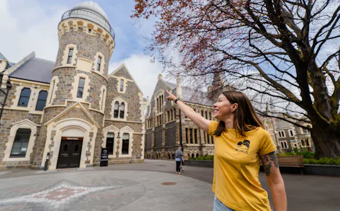 Person pointing at historic stone building in Christchurch during walking tour.