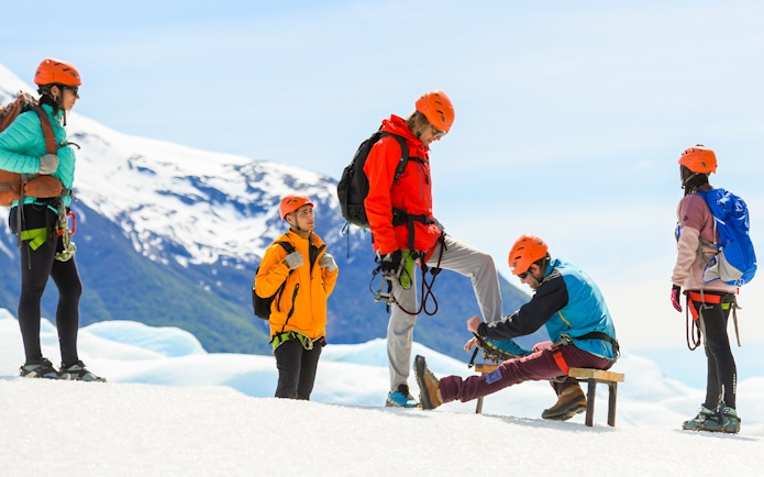 Guide assisting tourist with snow boots on Perito Moreno Glacier hike.