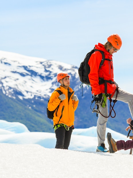 Guide assisting tourist with snow boots on Perito Moreno Glacier hike.