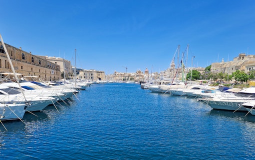 Boats docked in a marina with historic buildings in the background, part of the 3 Cities Tour.