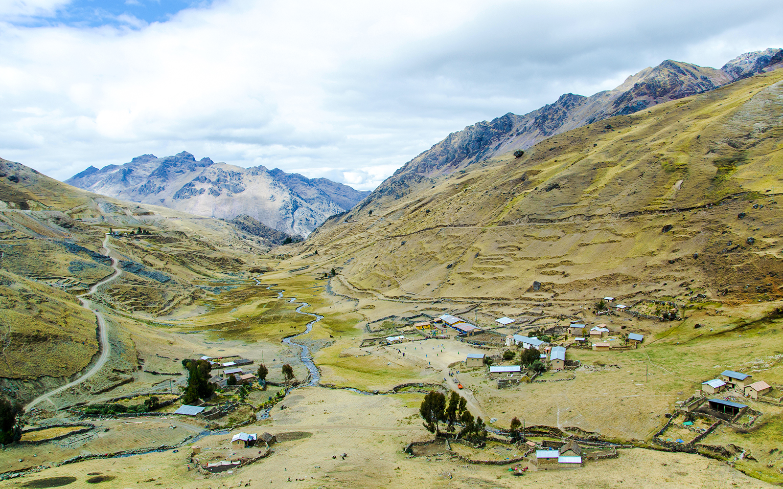 Small mountain village with scattered houses on Lares Trek, Peru, surrounded by hills and a winding stream.