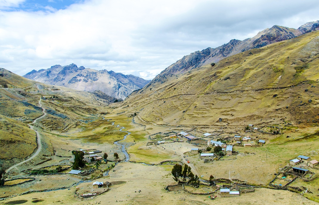 Small mountain village with scattered houses on Lares Trek, Peru, surrounded by hills and a winding stream.