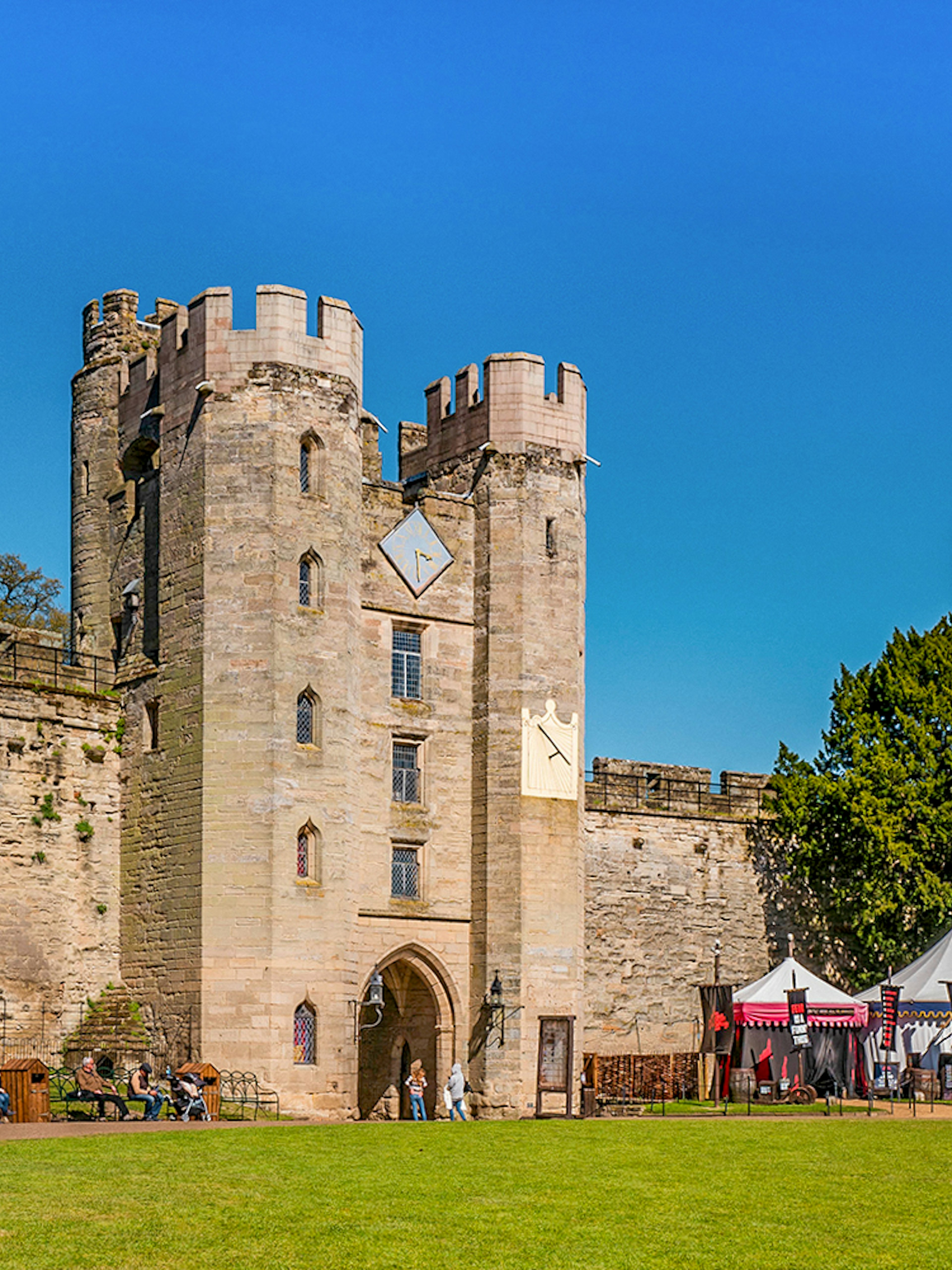Warwick Castle entrance with visitors and medieval tents on a sunny day.