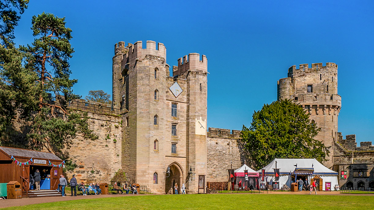Warwick Castle entrance with visitors and medieval tents on a sunny day.