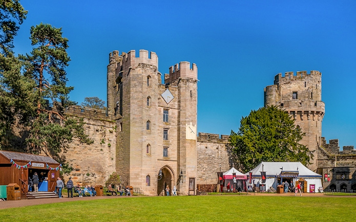 Warwick Castle entrance with visitors and medieval tents on a sunny day.