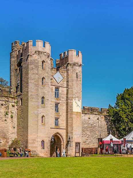 Warwick Castle entrance with visitors and medieval tents on a sunny day.