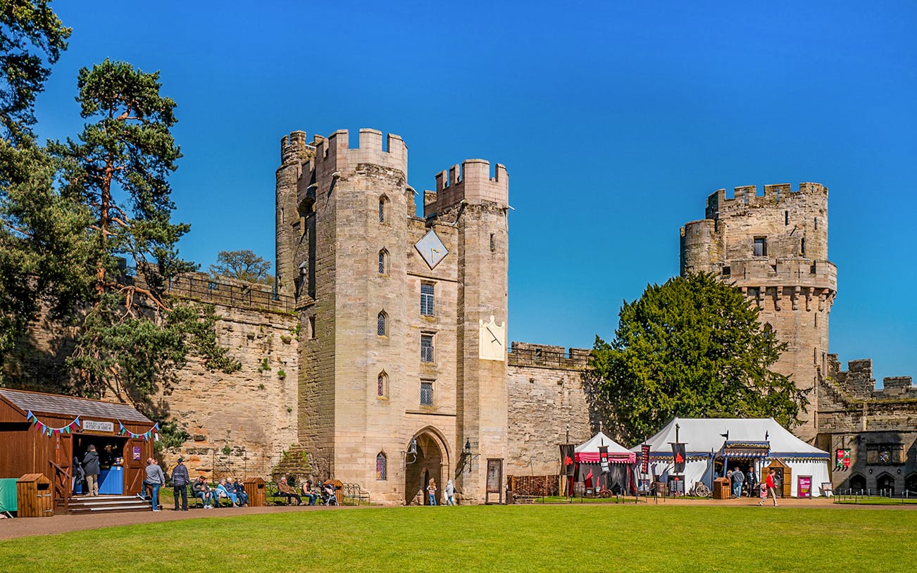 Warwick Castle entrance with visitors and medieval tents on a sunny day.