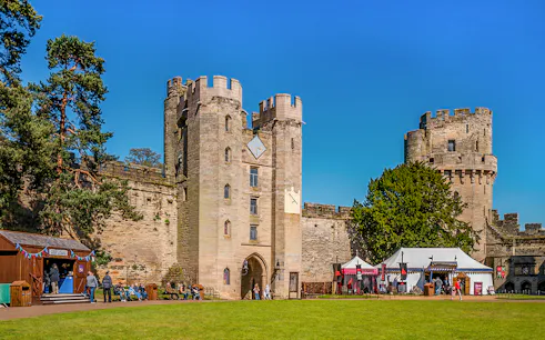 Warwick Castle entrance with visitors and medieval tents on a sunny day.