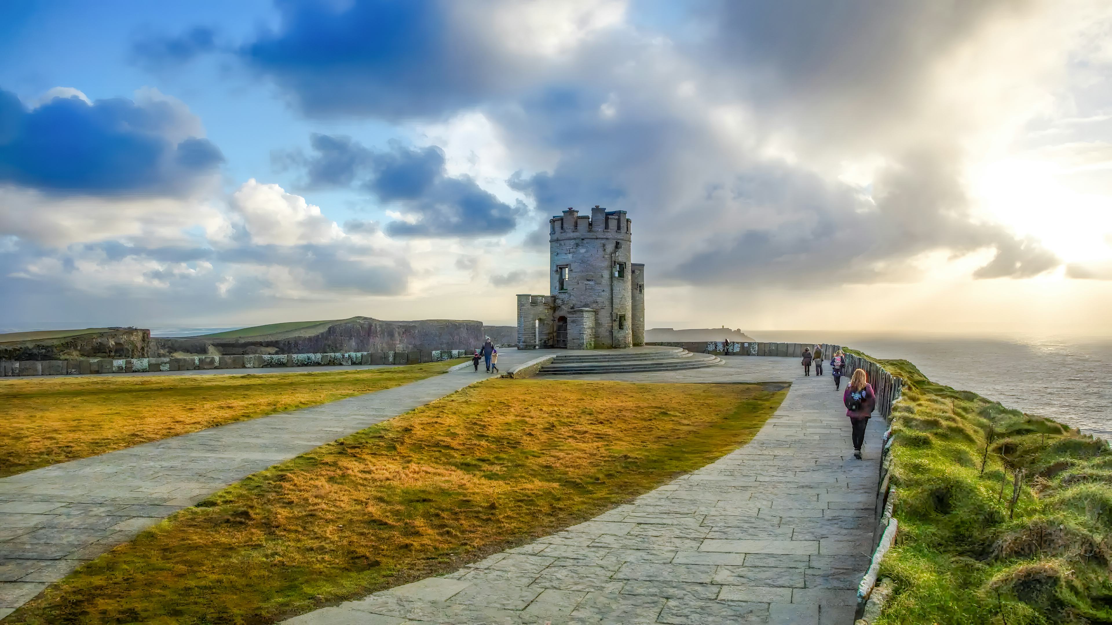tourists observing O'Brien's Tower at the Cliffs of Moher, Ireland, under a blue sky.