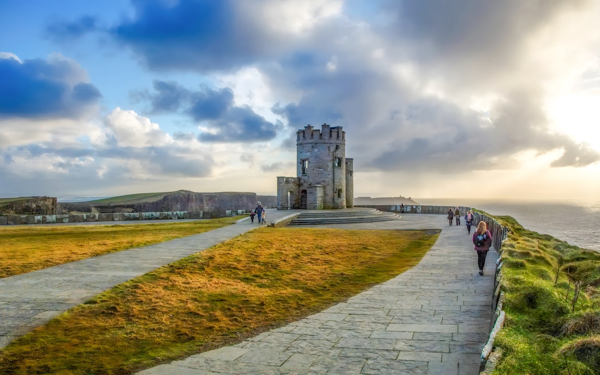 tourists observing O'Brien's Tower at the Cliffs of Moher, Ireland, under a blue sky.