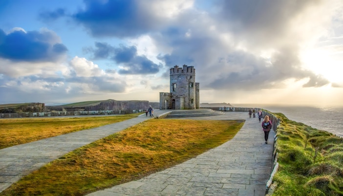 tourists observing O'Brien's Tower at the Cliffs of Moher, Ireland, under a blue sky.