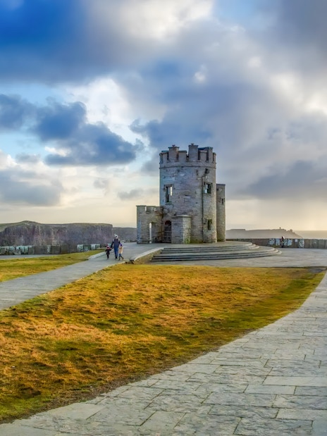 tourists observing O'Brien's Tower at the Cliffs of Moher, Ireland, under a blue sky.