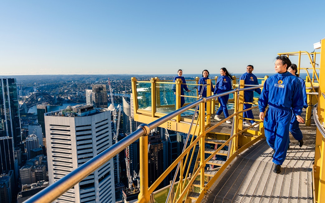 Group walking on Sydney Tower Eye Skywalk with city skyline view.