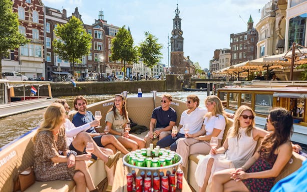 Amsterdam canal cruise boat on water with passengers enjoying Red Light District views.