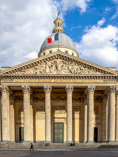 Pantheon in Paris with neoclassical facade and French flag on dome.