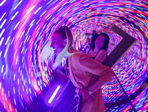 Visitors enjoying the colorful vortex tunnel at Museum of Illusions Seville.