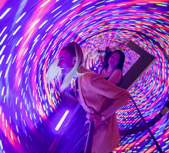 Visitors enjoying the colorful vortex tunnel at Museum of Illusions Seville.