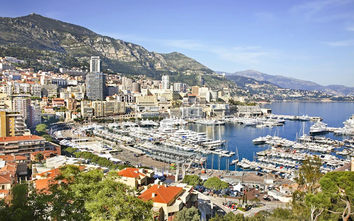 Monte Carlo harbor with yachts and cityscape against mountain backdrop.