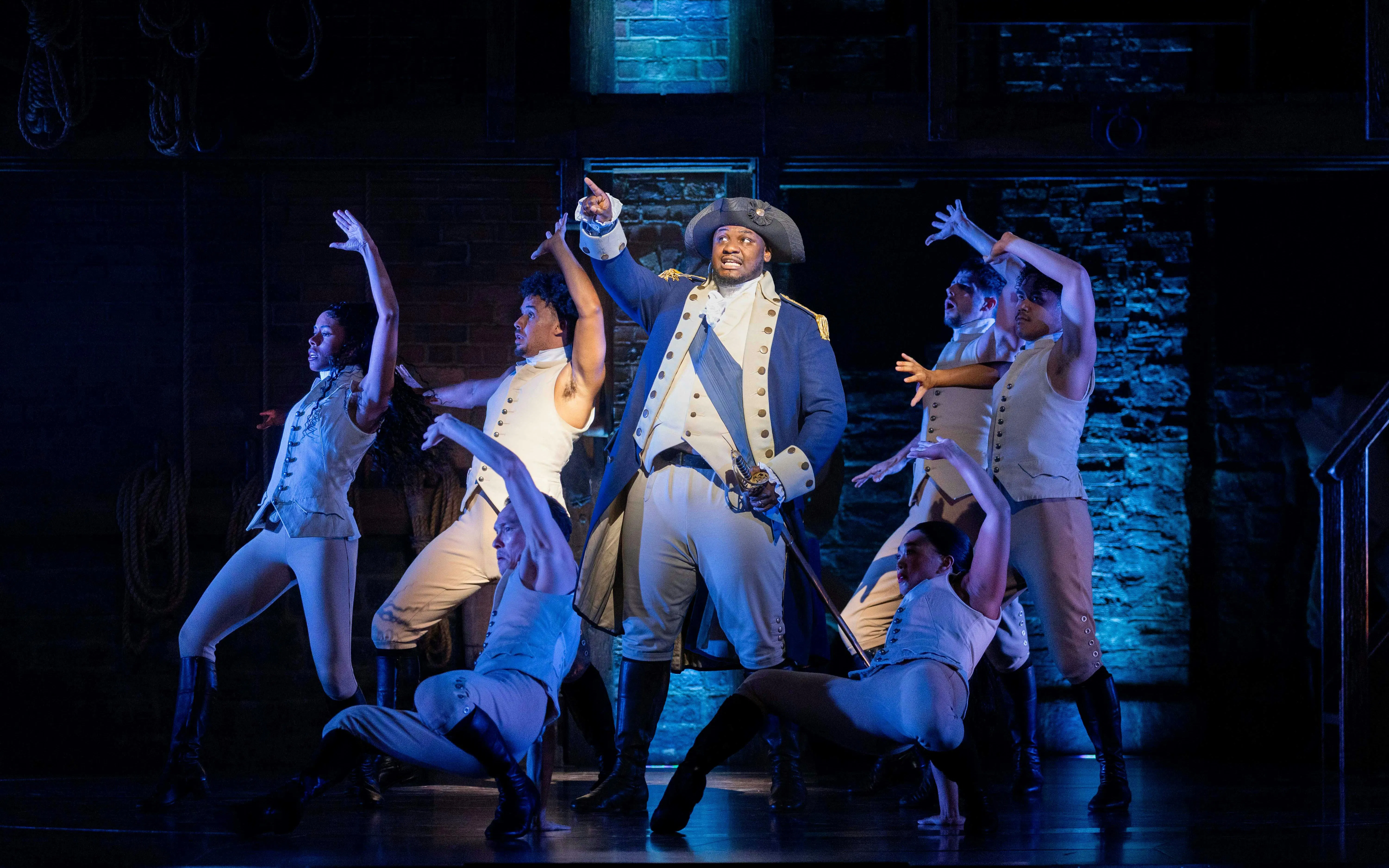 Hamilton cast performing on West End stage, actors in period costumes.