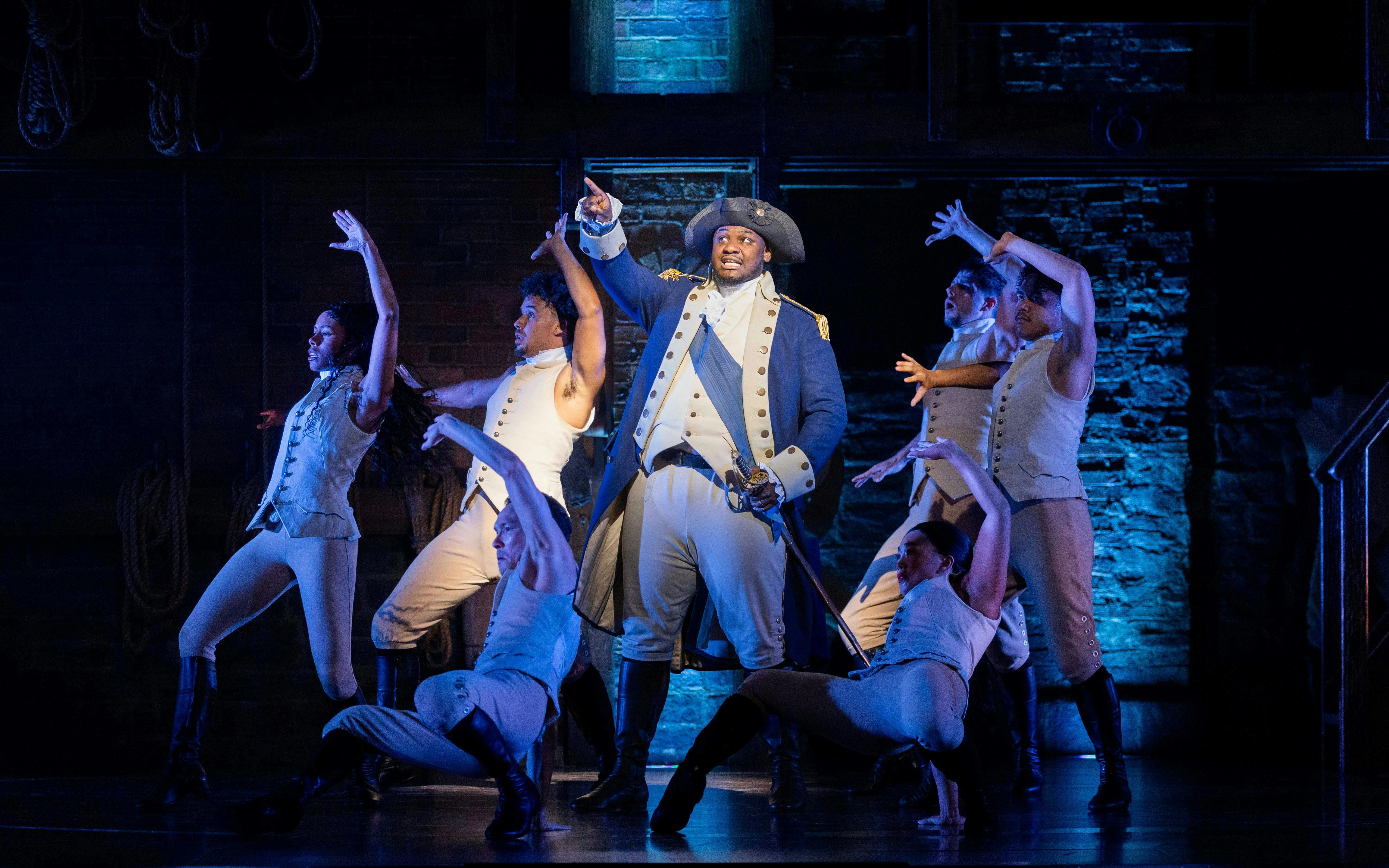 Hamilton cast performing on West End stage, actors in period costumes.