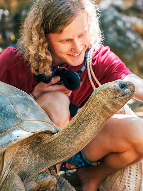 Tourist taking a selfie with an Aldabra Tortoise in a natural setting.