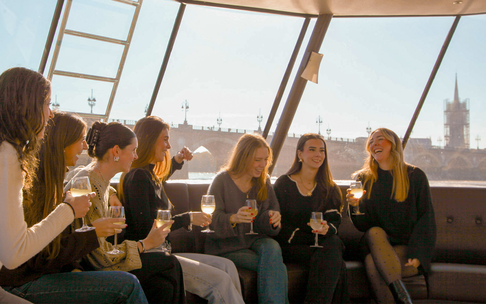 Group enjoying wine on a Bordeaux river cruise with cityscape in background.
