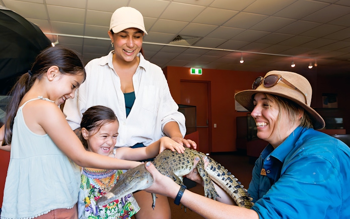 Guests at Crocosaurus Cove petting a baby crocodile indoors.