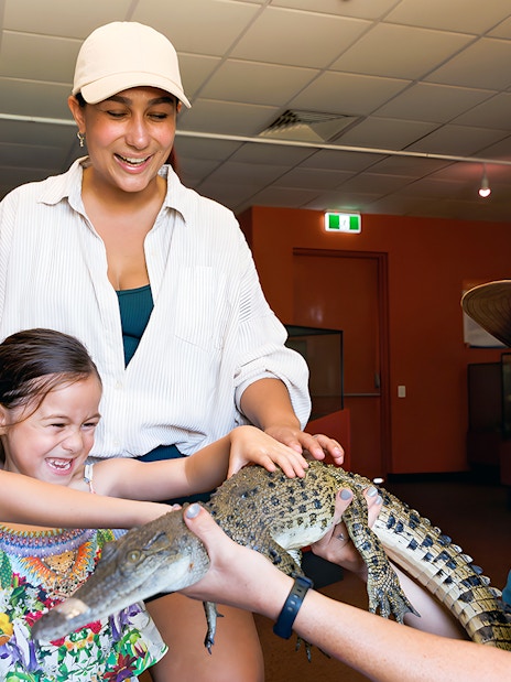 Guests at Crocosaurus Cove petting a baby crocodile indoors.