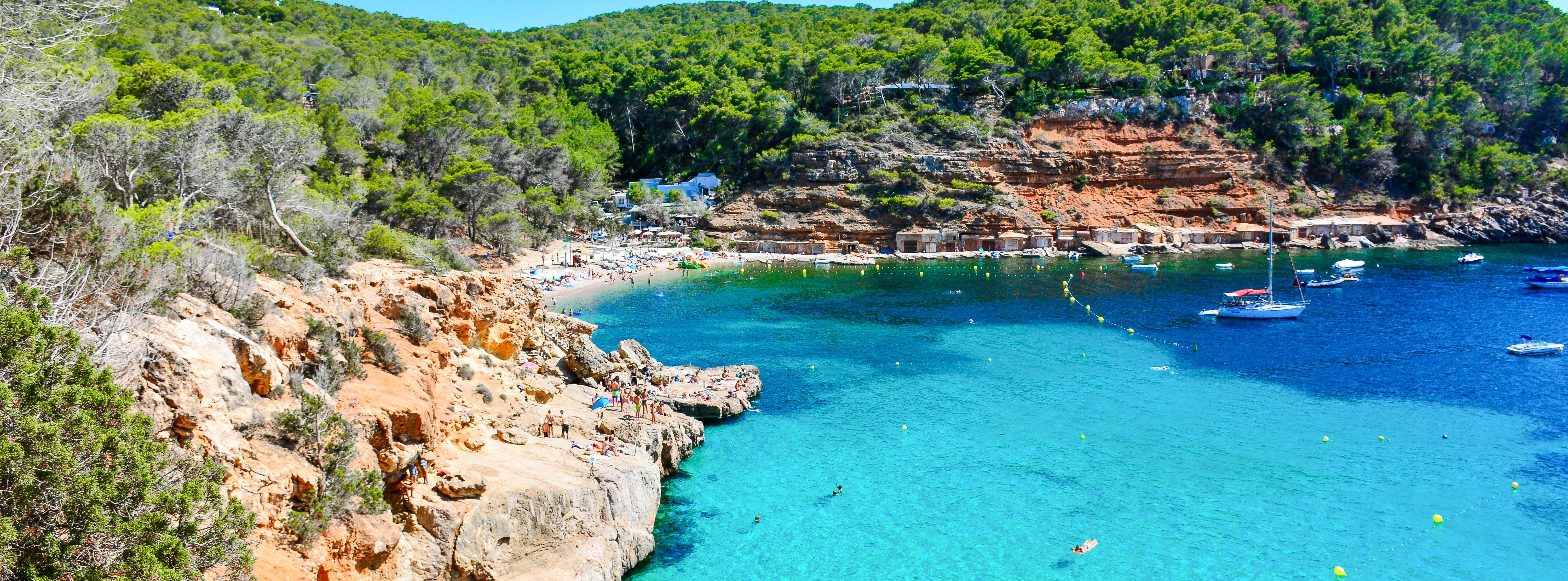 Tourists sunbathing on a sandy beach in Ibiza, Spain with clear blue waters.