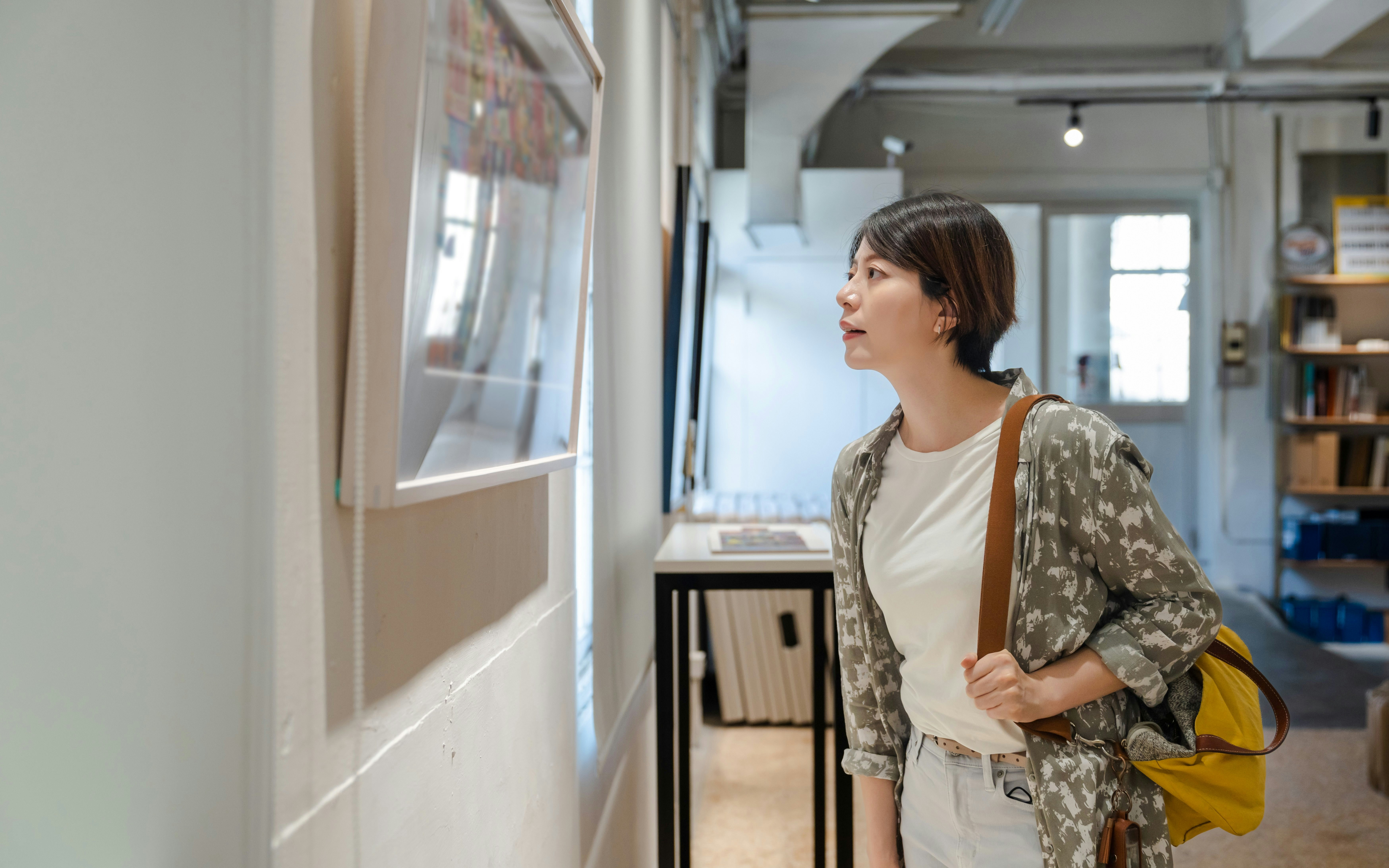 Asian woman viewing framed paintings in a gallery.