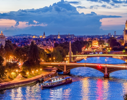 Paris skyline at night with Seine river and Paris En Scène Dinner Cruise boat.