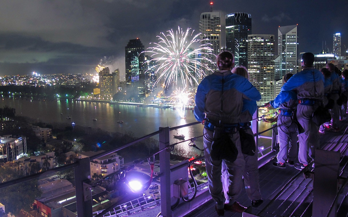 Climbers on Brisbane Story Bridge watching fireworks over the city at twilight.
