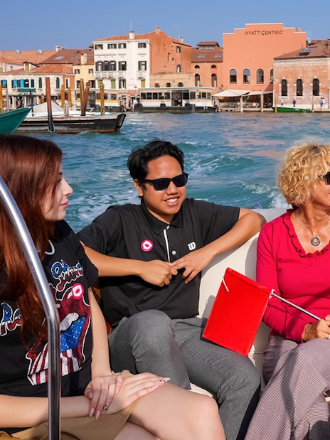 Tourists enjoying a boat ride in Venice with historic buildings in the background.