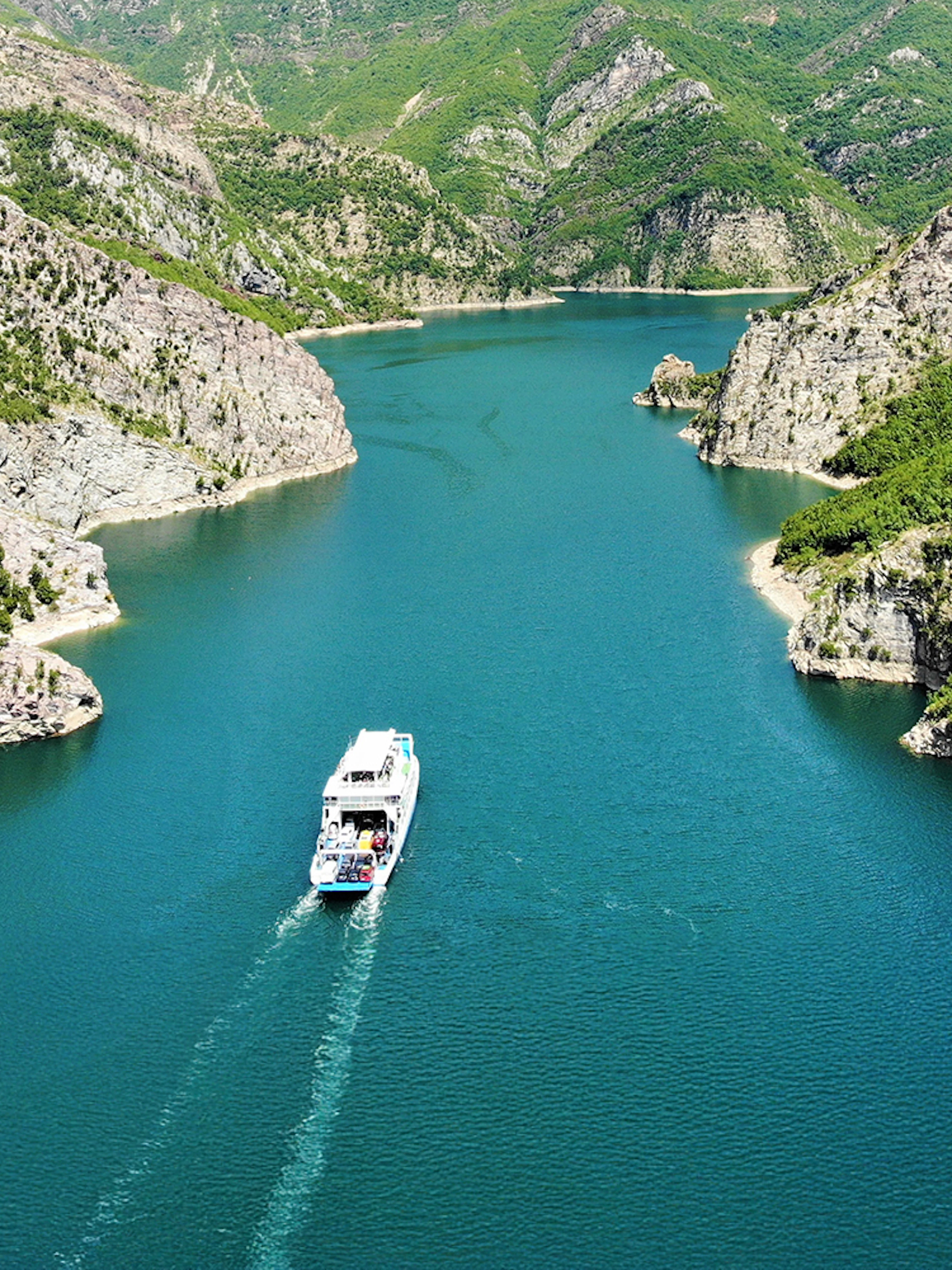 Boat cruising through Komani Lake surrounded by lush mountains on Shala River Day Trip.