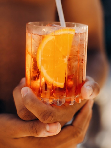 Man holding an Aperol Spritz cocktail with an orange slice.