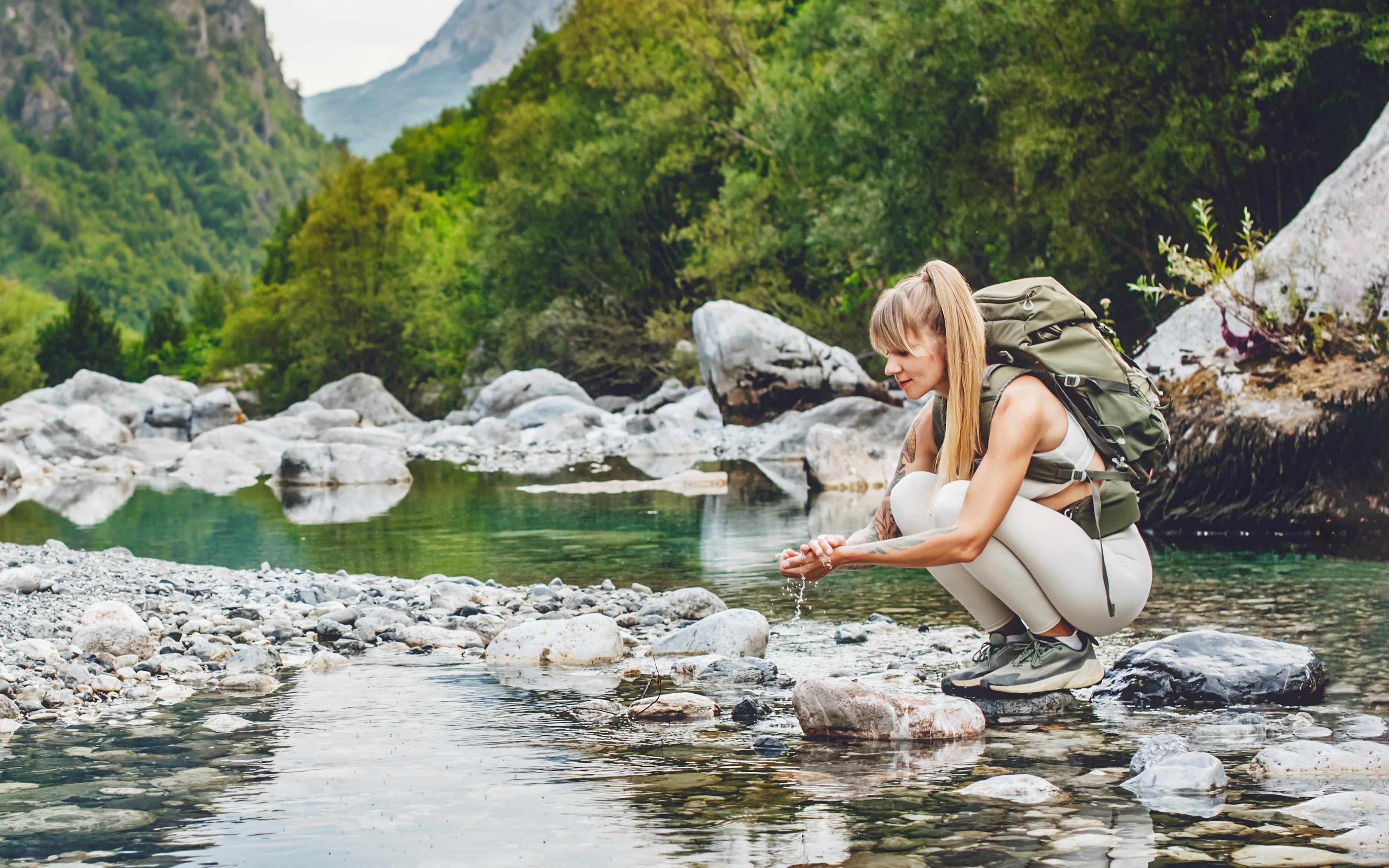 Woman tourist washing hands in Shala River, surrounded by rocky landscape and greenery.