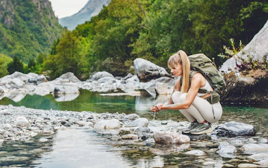 Woman tourist washing hands in Shala River, surrounded by rocky landscape and greenery.